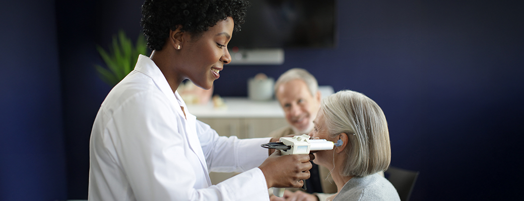Image of a female hearing care professional using a tool to examine the ear of a senior woman